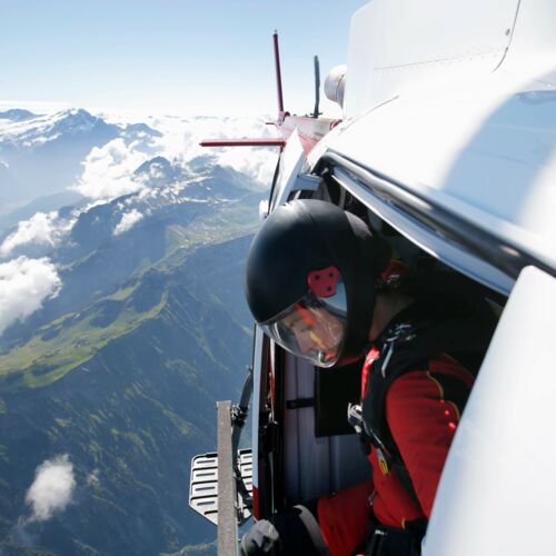 Female sky diver in helicopter checking for exit over mountain.